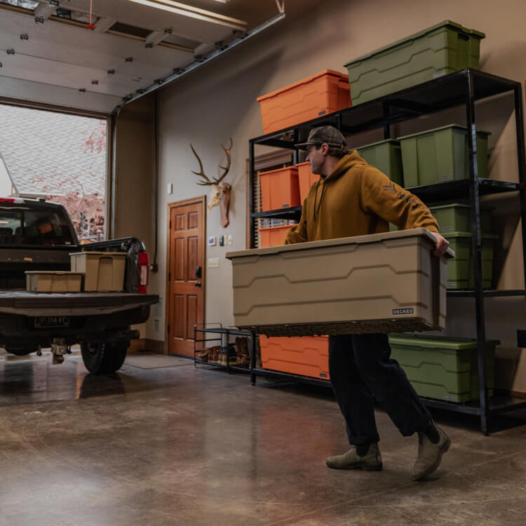 Person moving a large Payloader 133 storage bin into a garage with a truck and storage shelves in the background.