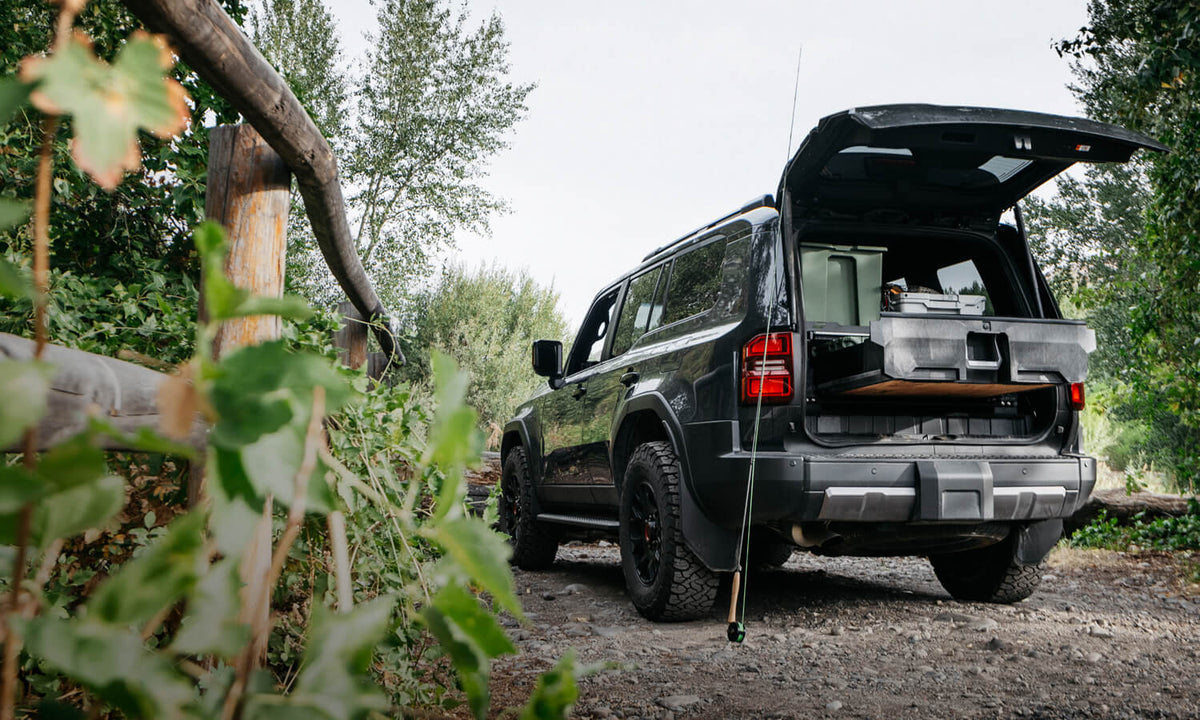 Black Toyota Land cruise parked next to the river with a DECKED drawer system installed in the back if it with fishing gear.