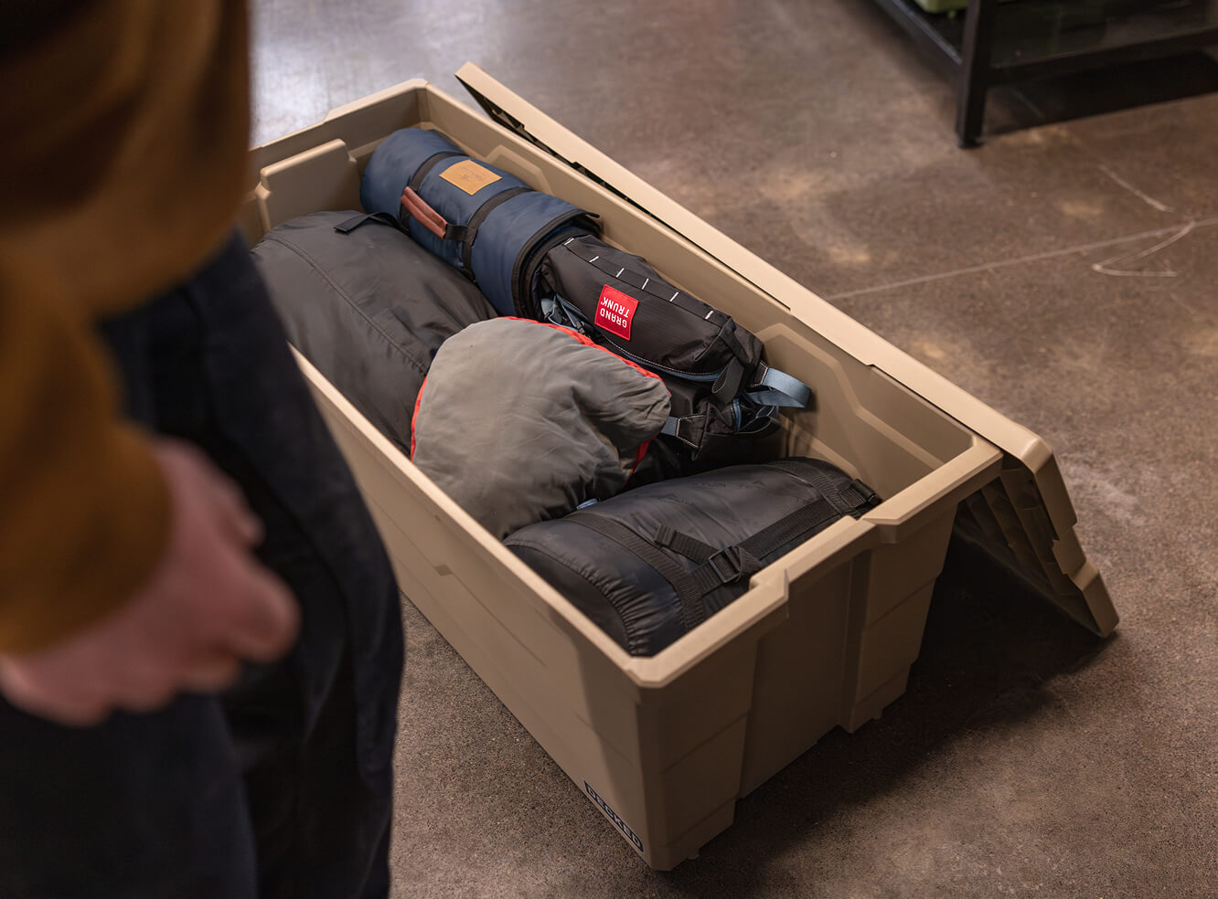 Person looking at a Desert Tan Payloader 133 storage container filled with camping gear on a concrete floor