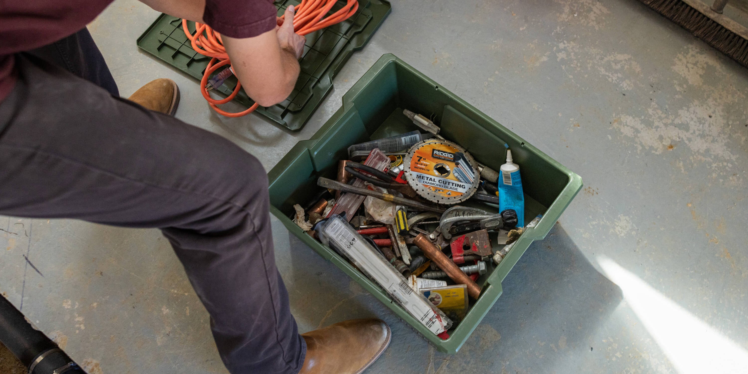 Person organizing extension cords and tools in a ranger green Payloader bin on a concrete floor.
