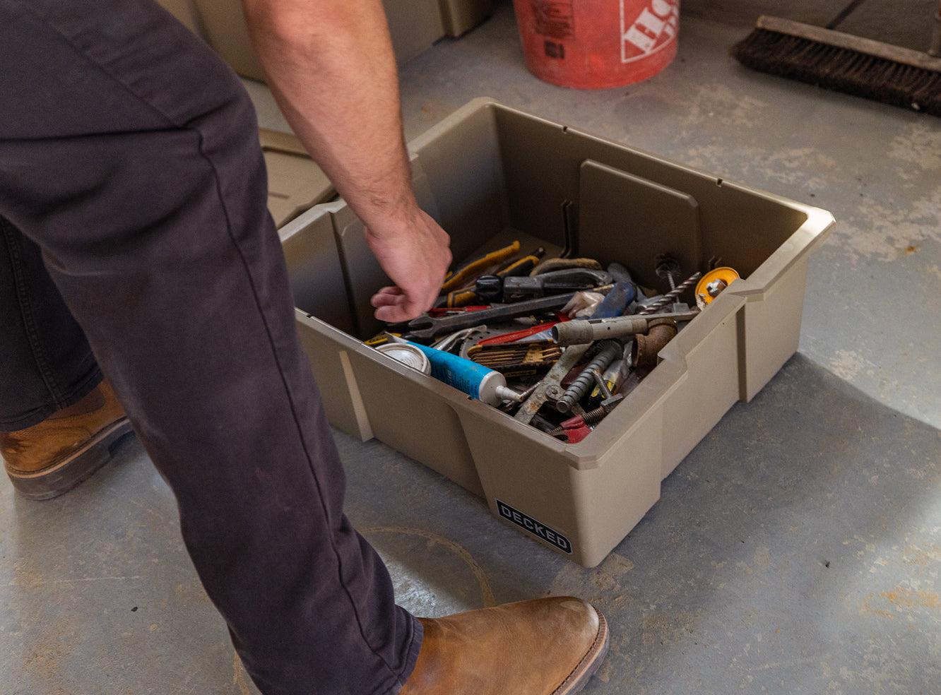 Person reaching into a Payloader 32 Bin filled with tools on a concrete floor.