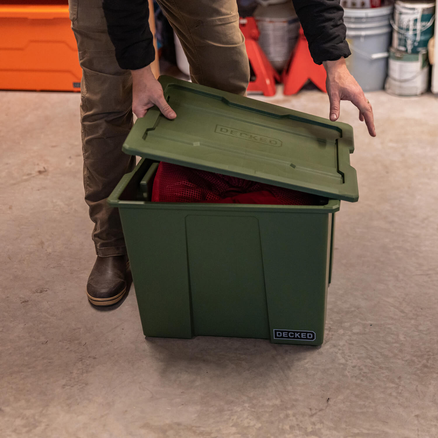 A person putting a lid on his ranger green Payloader 64 bin full of camping supplies.