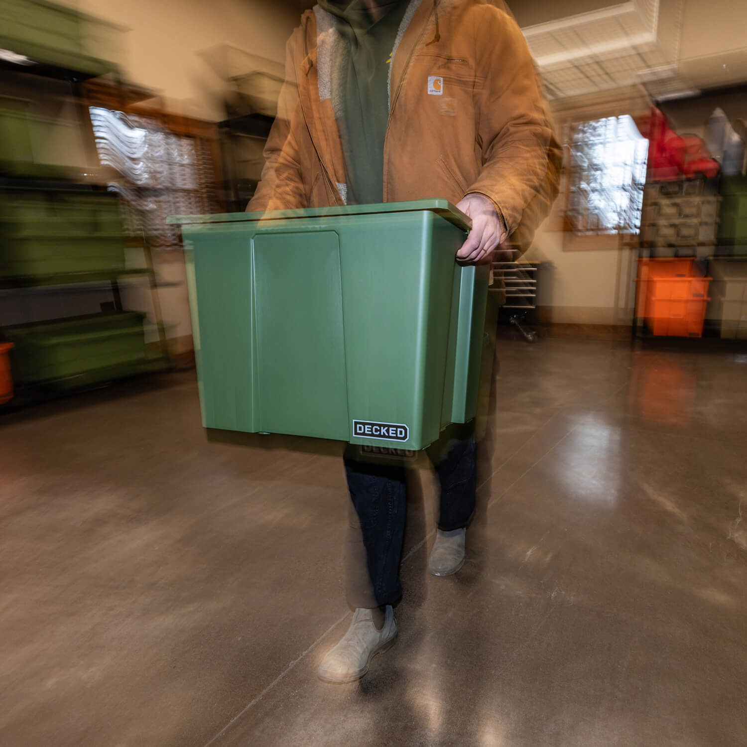 A blurry image of a man transporting a ranger green Payloader 64 Bin from the racks in his garage to his truck.