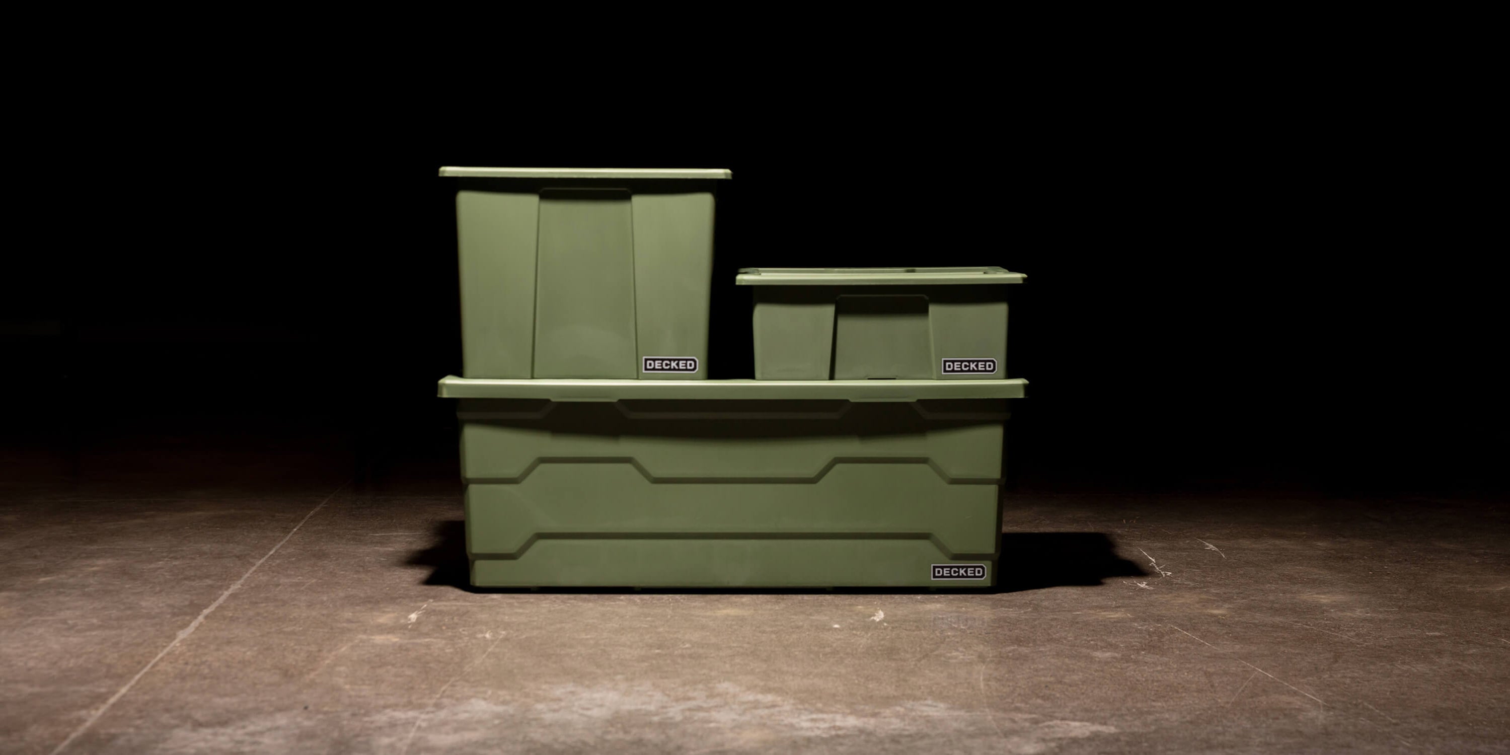 Three ranger green Payloader Bin sizes stacked on top of each other in a garage with a dark, shadowy background.