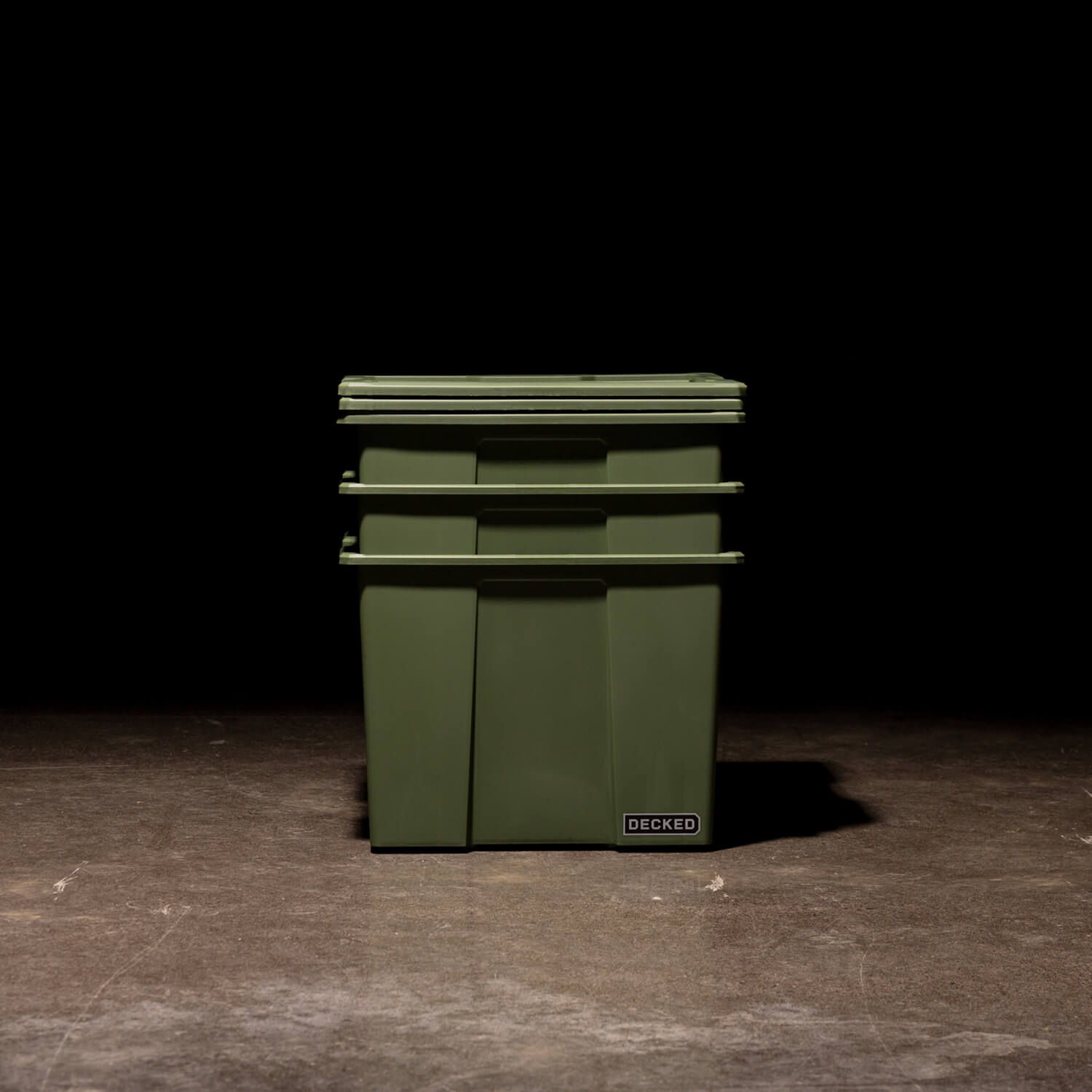Three ranger green Payloader 64 Bins nested together with the lids sitting on top in a garage with a dark, shadowy background.