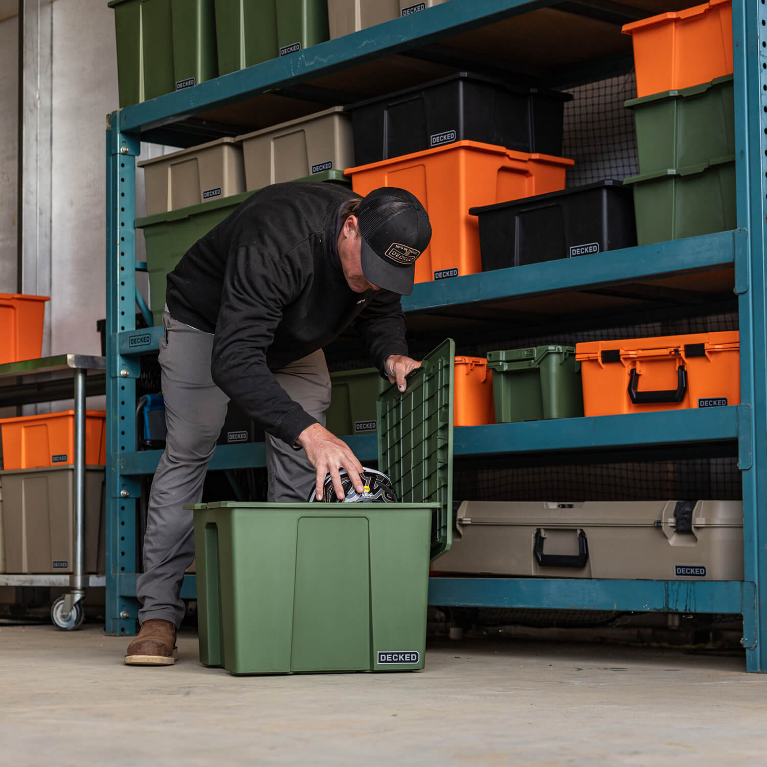 A man putting a bike helmet into a Payloader 64 bin with a storage rack and plenty of DECKED bins and cases behind him.