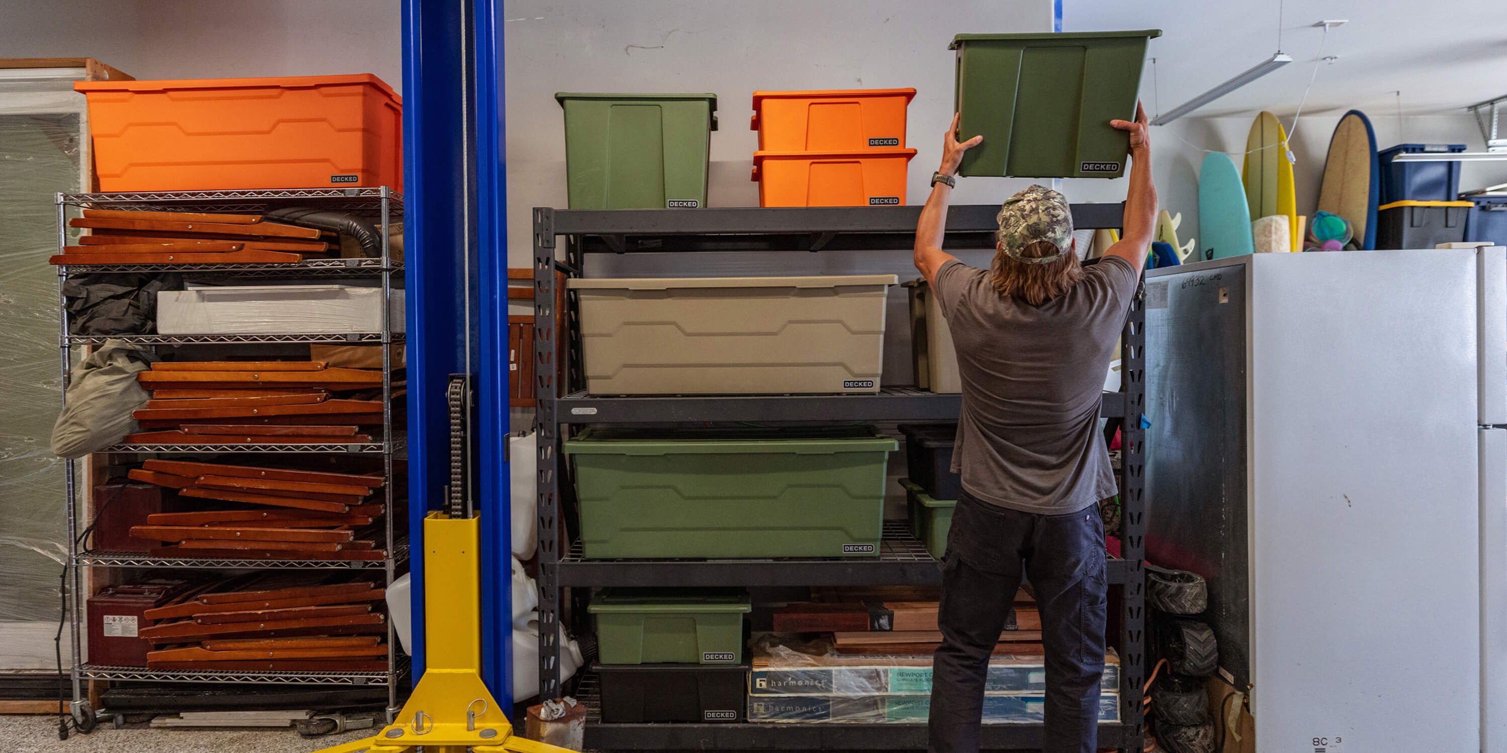 A man retrieving a DECKED ranger green Payloader 64 Bin from the top shelf of a storage rack in a garage.