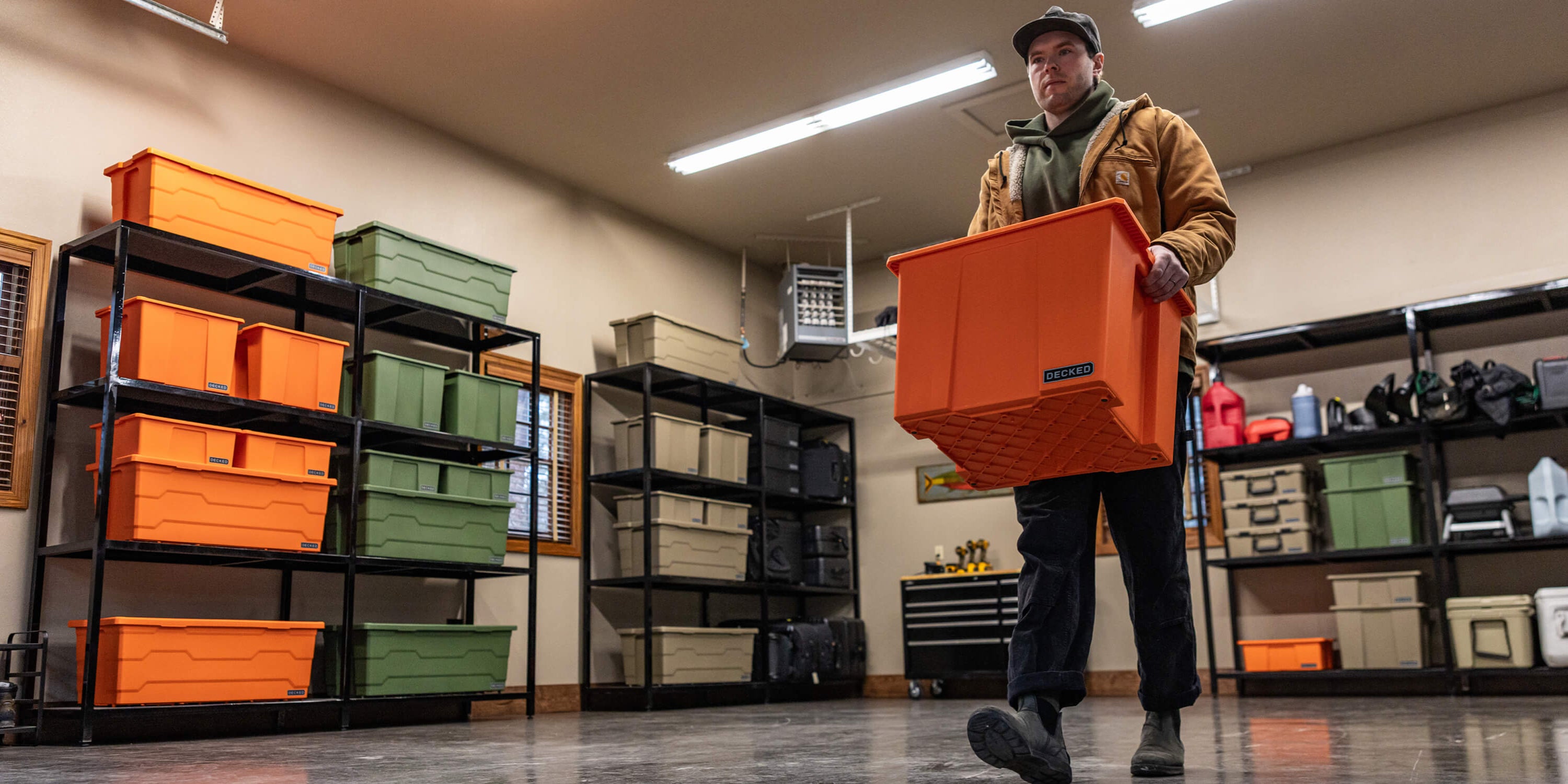 A man carrying a blaze orange Payloader 64 from the racks in his garage to his truck.