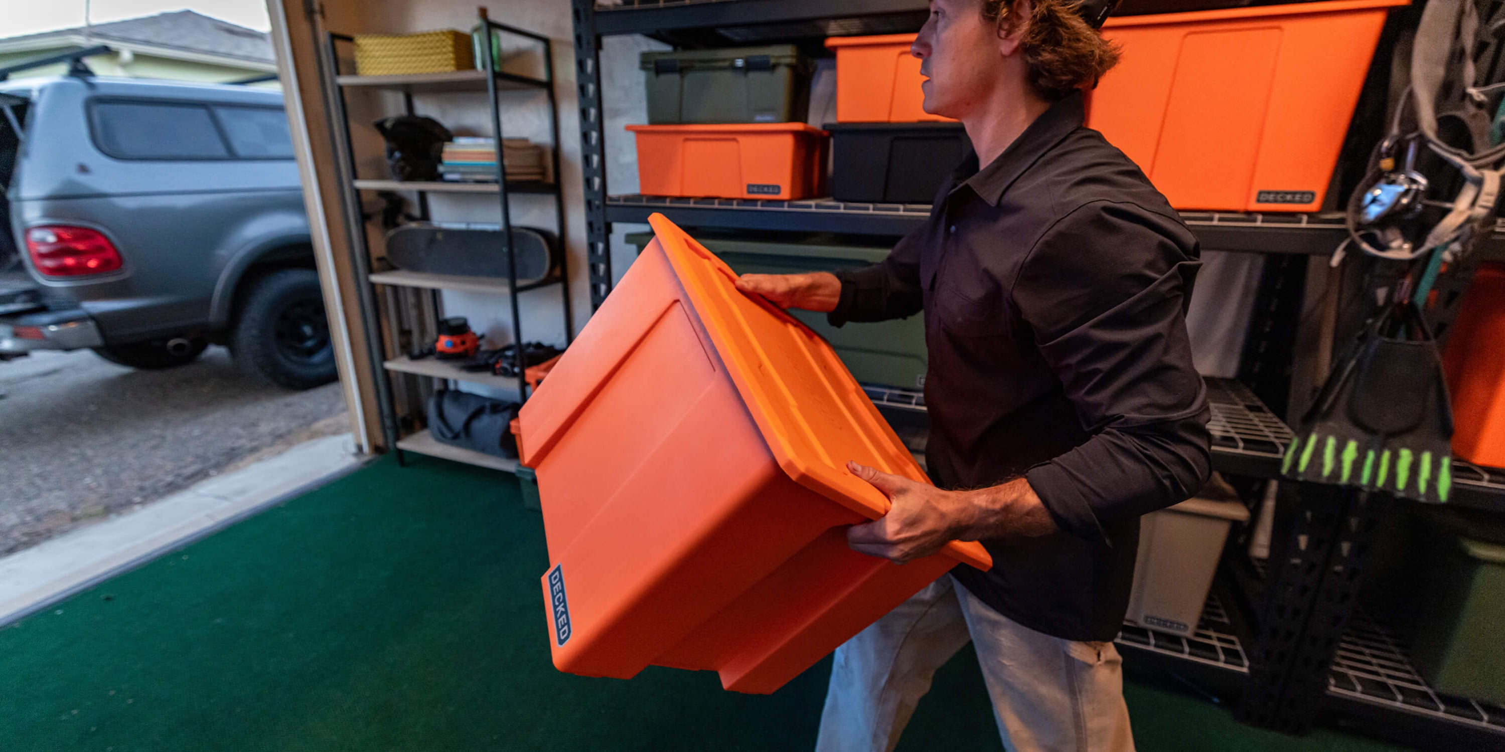 A man carrying a blaze orange Payloader 64 Bin from the storage racks in his garage to his truck.