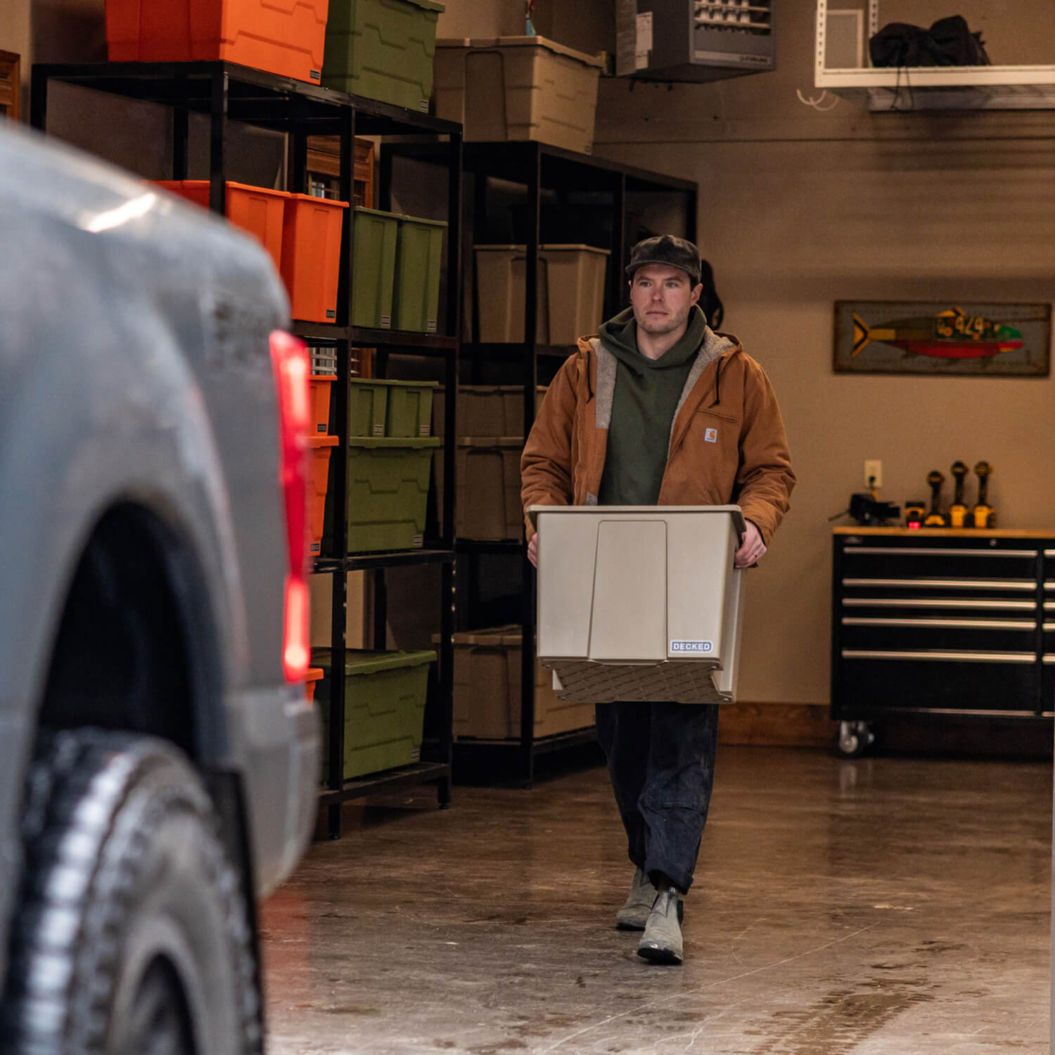 A man in a Carhartt jacket carrying a Payloader 64 rugged bin from his garage shelving to his truck.