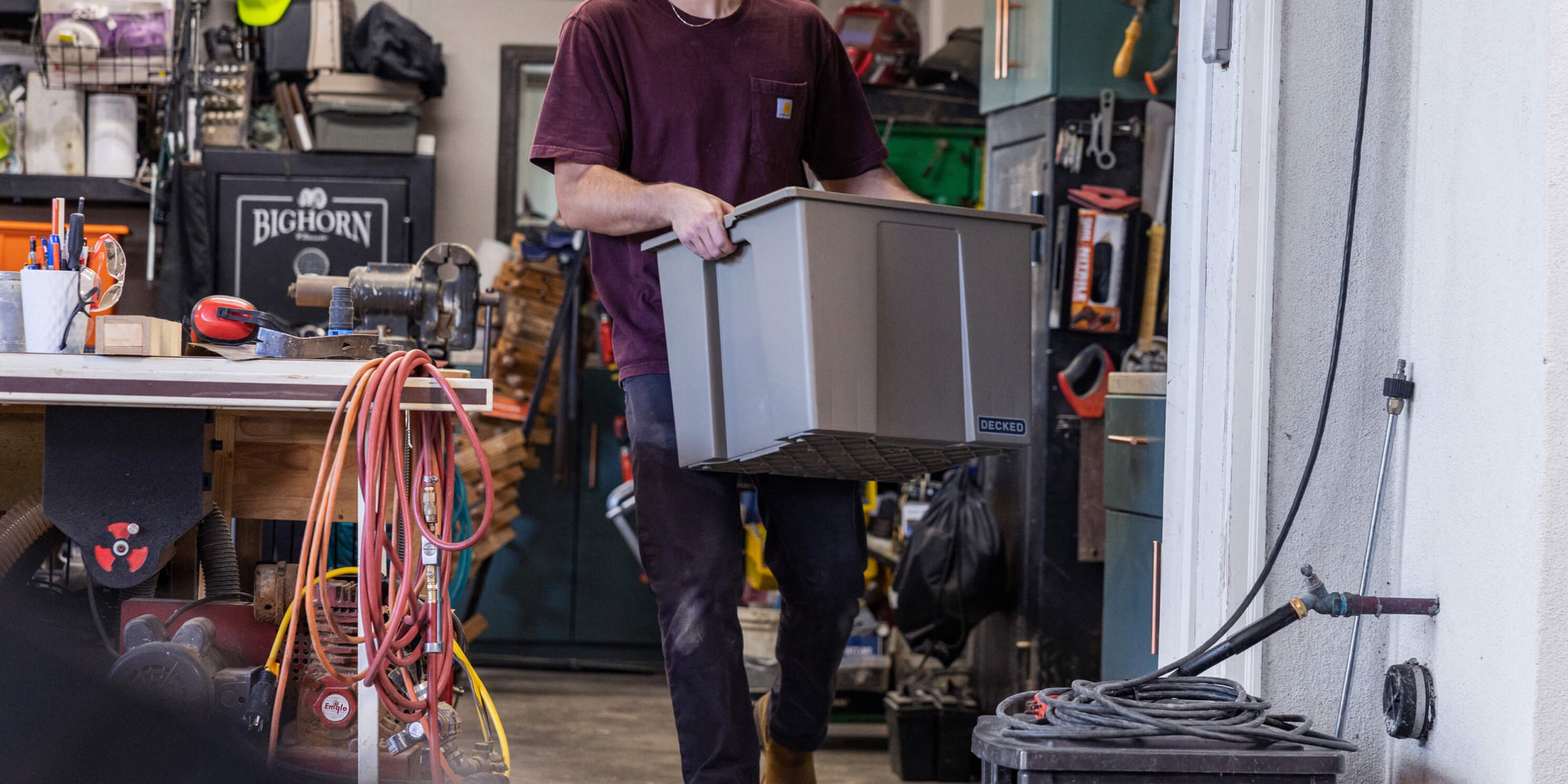 A man carrying a DECKED Payloader 64 Bin through his workshop.