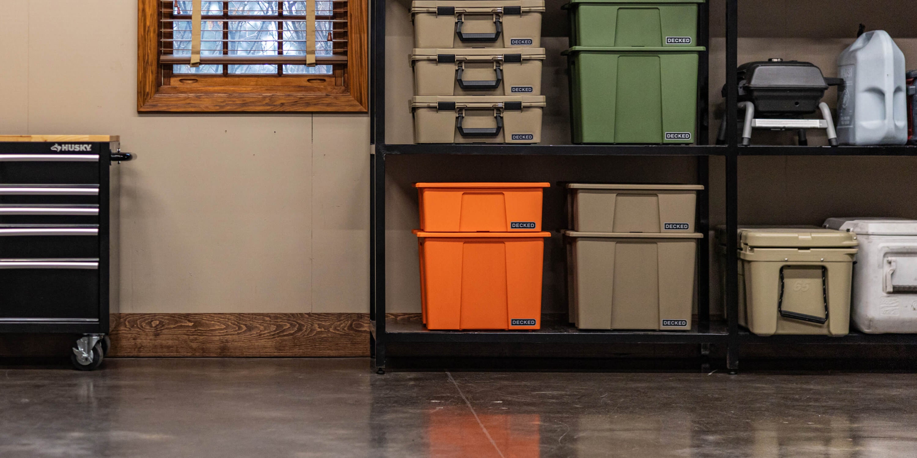Various Payloader Bin sizes and other protective cases with DECKED branding, stacked on one another on shelving in a garage.