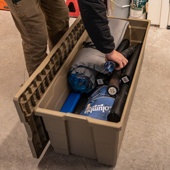 Person organizing items in a large Desert Tan Payloader 133 storage bin with a blue cooler and black bag.