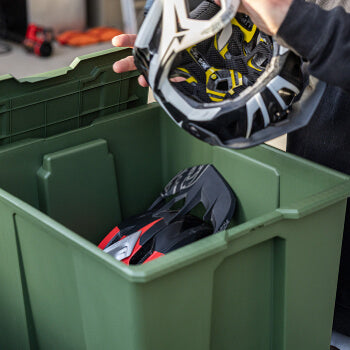 Person placing a helmet into a green Payloader 64 bin with other items.