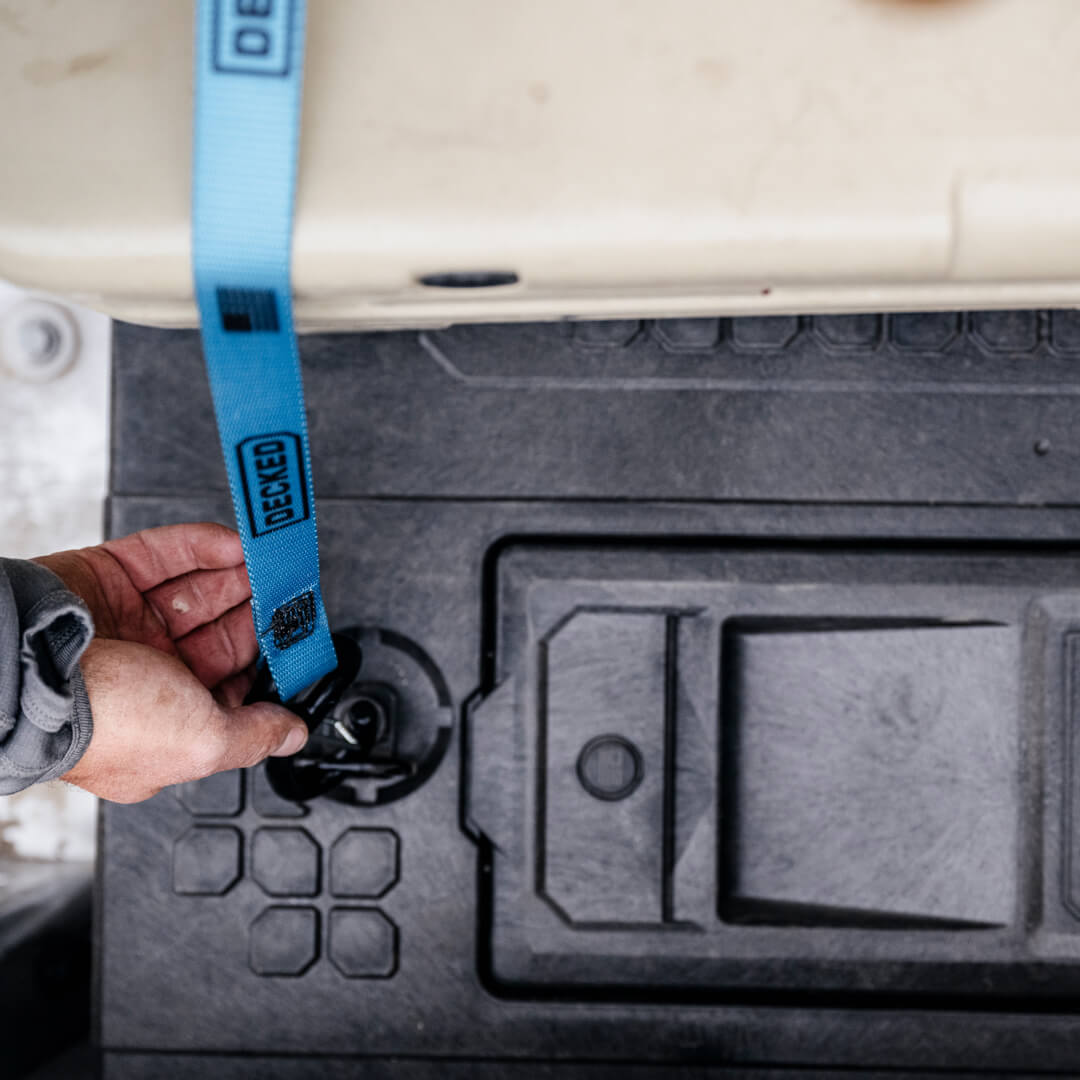 Blue ratchet strap being clipped to a Drawer System D-Ring to lash down a Yeti cooler.