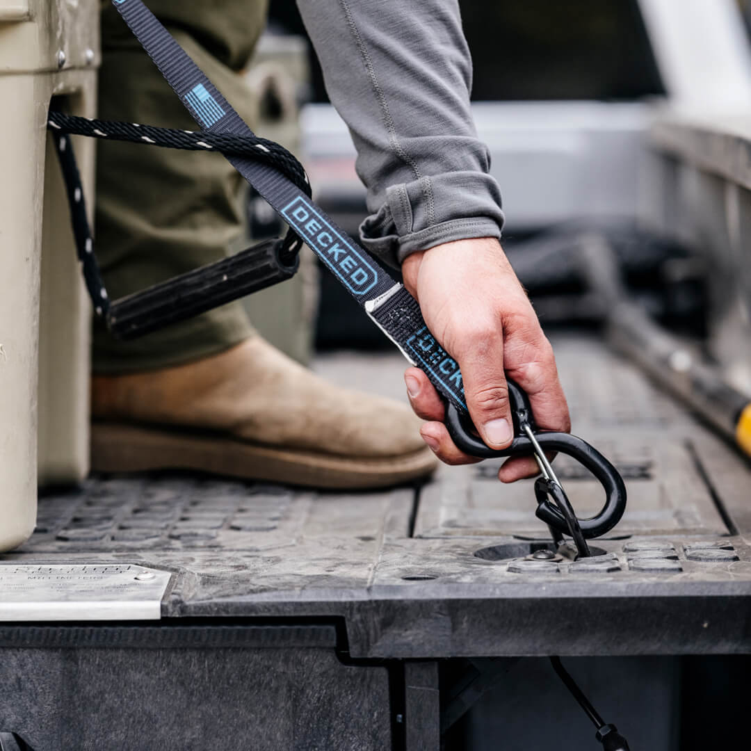 Black ratchet strap being clipped to a Drawer System D-Ring to lash down a Yeti cooler.