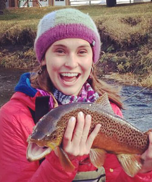 Woman smiling holding up a trout while fishing