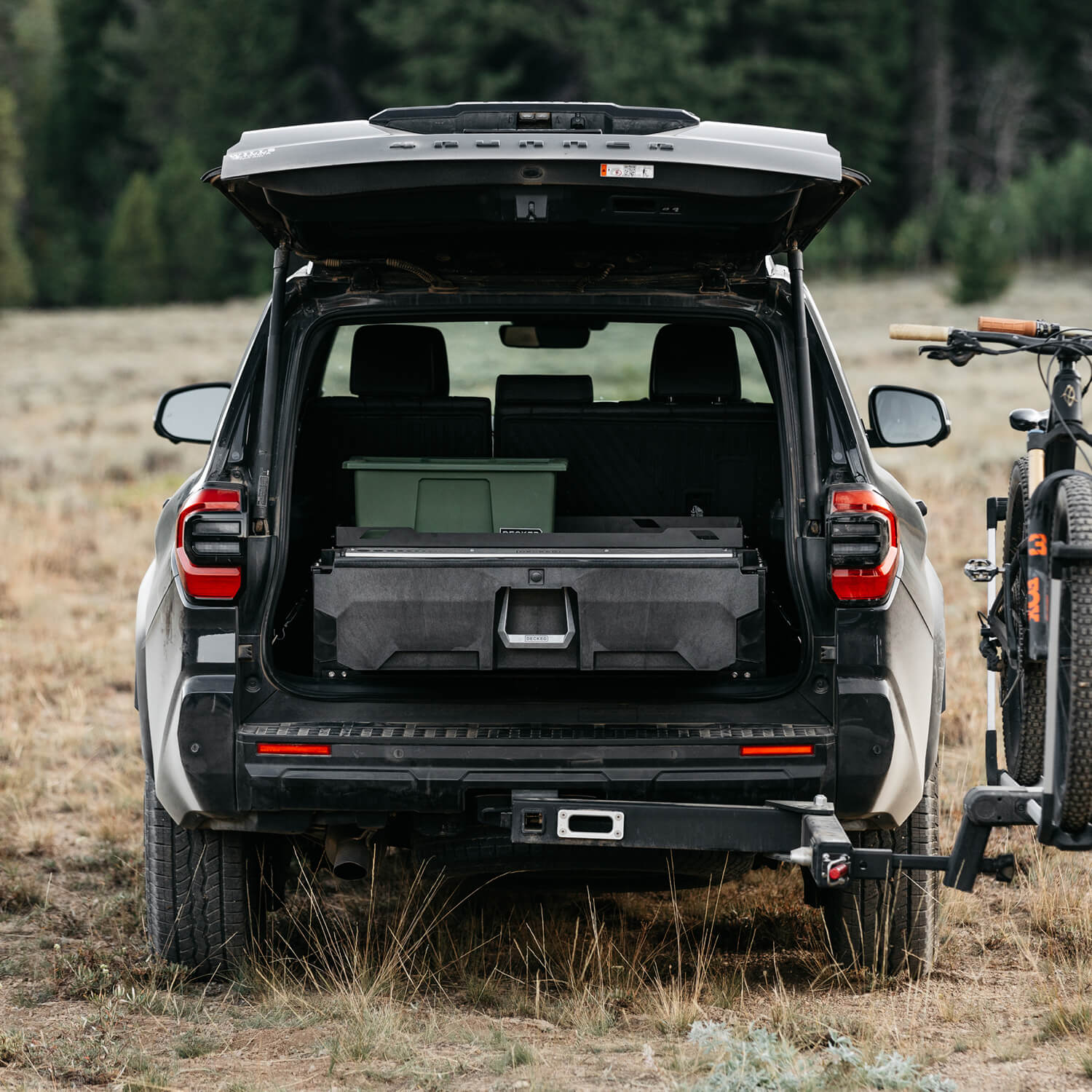 The open tailgate of a 4Runner with a DECKED Drawer System and rugged bin inside. The SUV is in a forest landscape with a bike rack and bikes nearby.