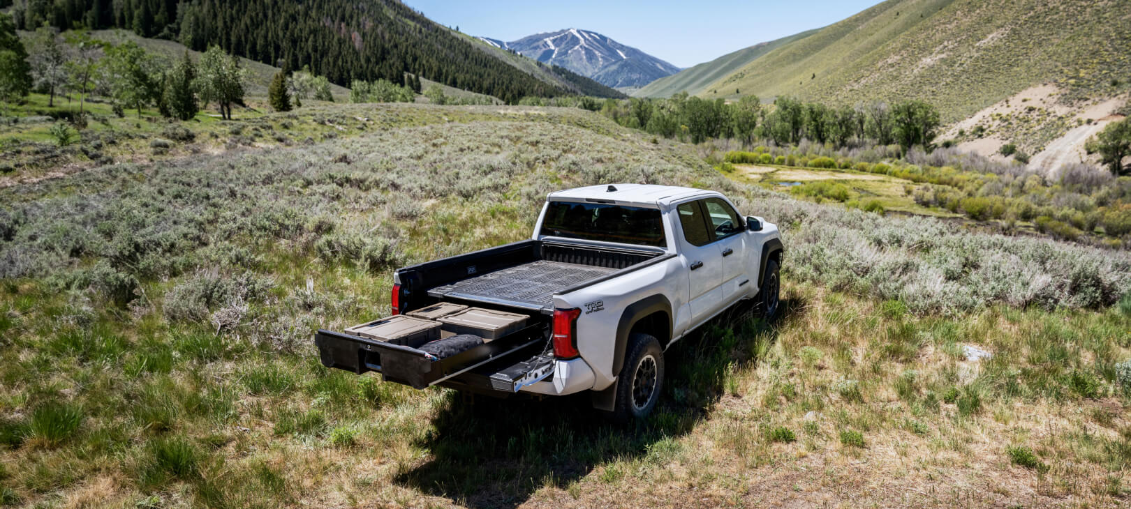 Wide view of a Toyota Tacoma's midsize Drawer System extended with a scenic mountain view in the background.