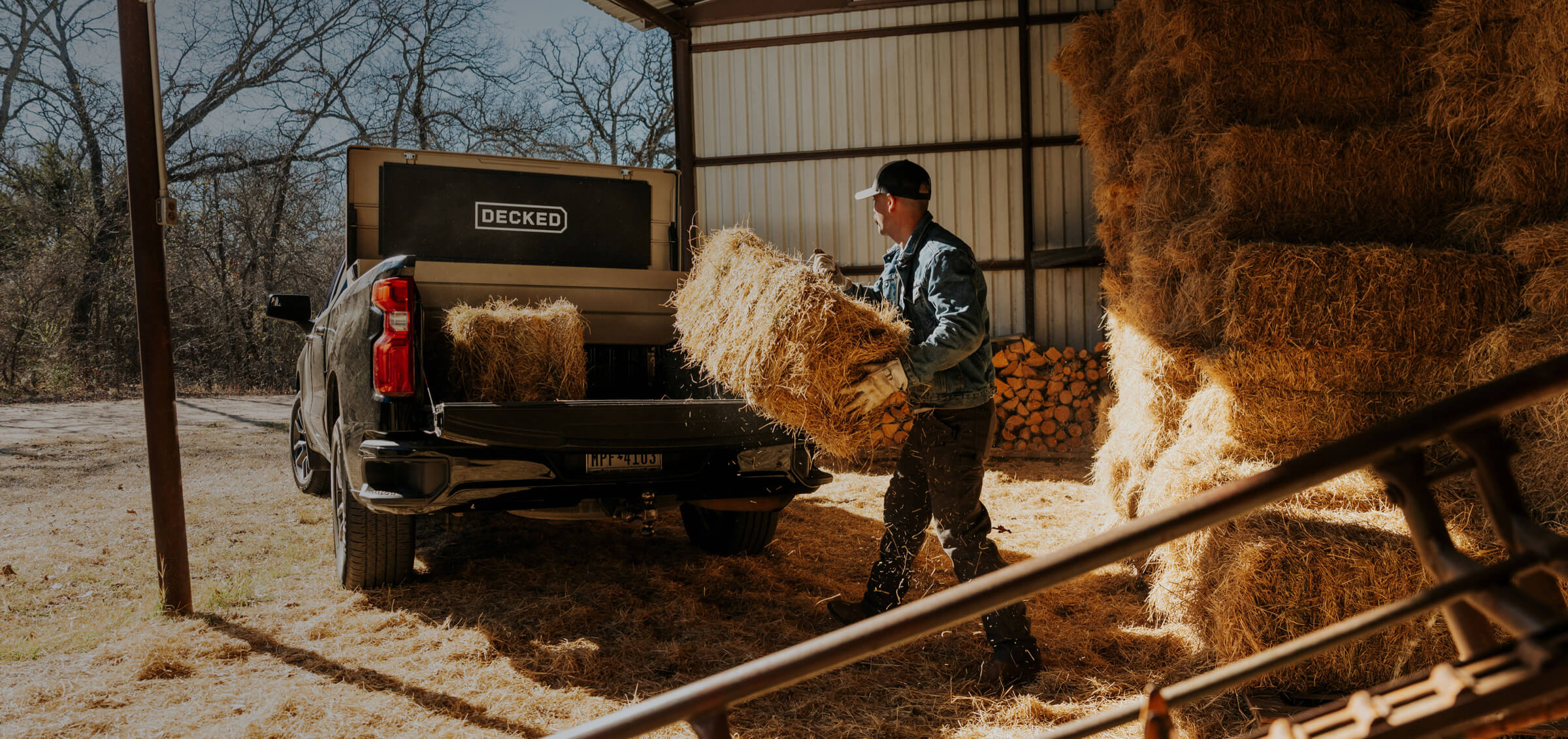 Person loading hay into a truck bed with a DECKED Tool Box inside in a barn setting.