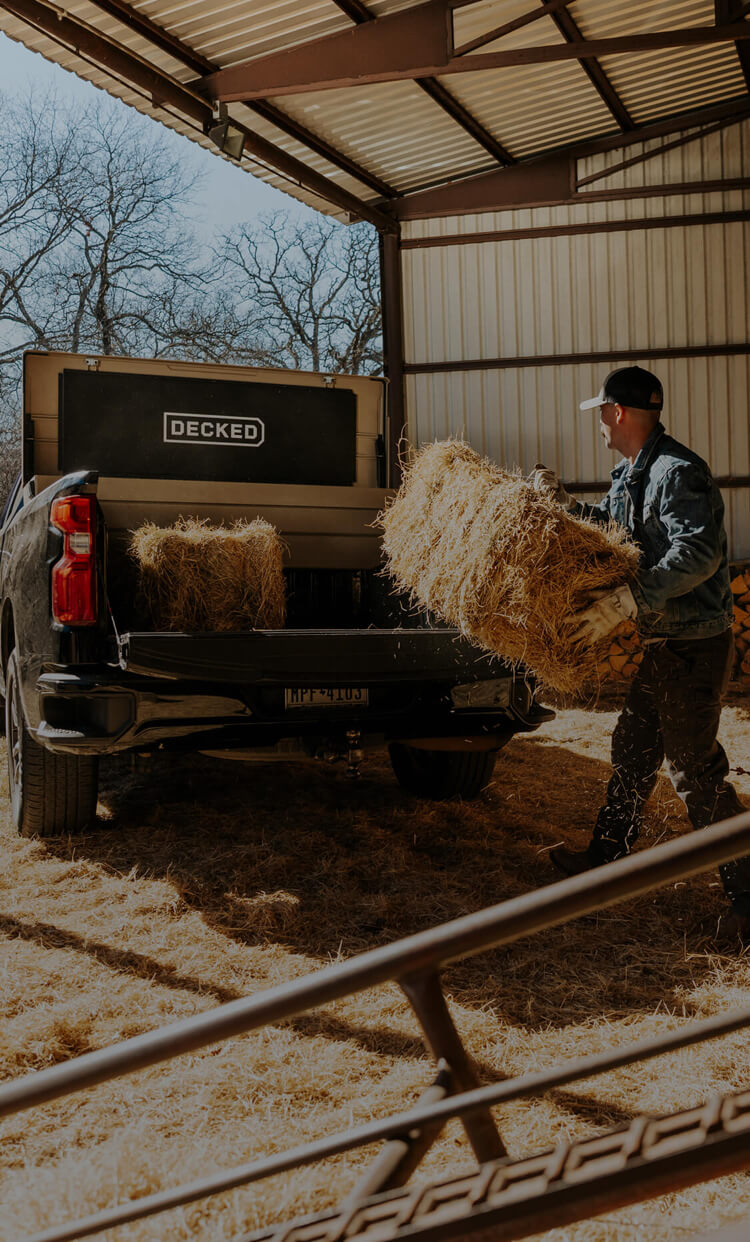 Person loading hay into a truck bed with a DECKED Tool Box inside in a barn setting.