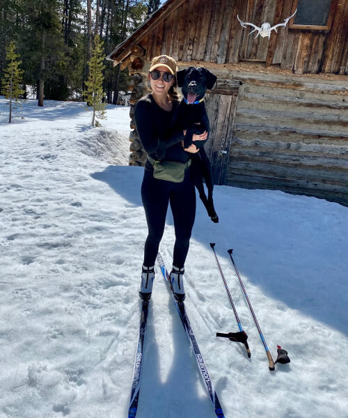 Woman cross country skiing holding up a black lab
