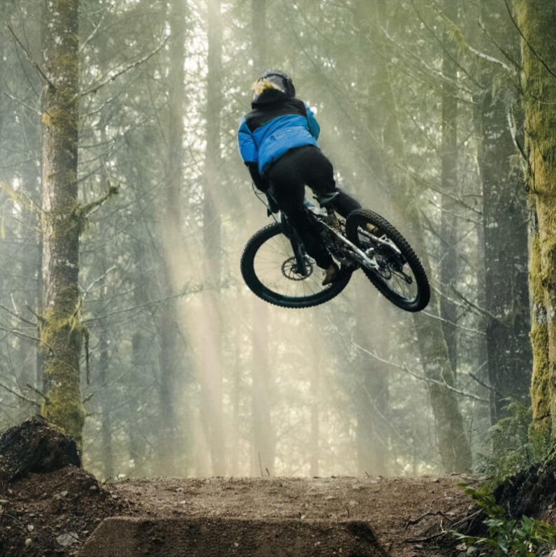 Casey Brown on a mountain bike in mid-air over a log jump in a forest
