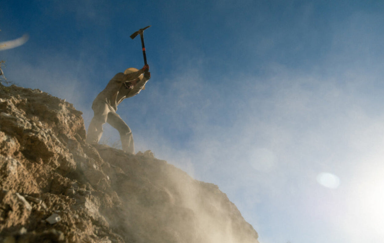 Casey Brown putting in work on rocks with a pick axe, making way for her mountain bike.