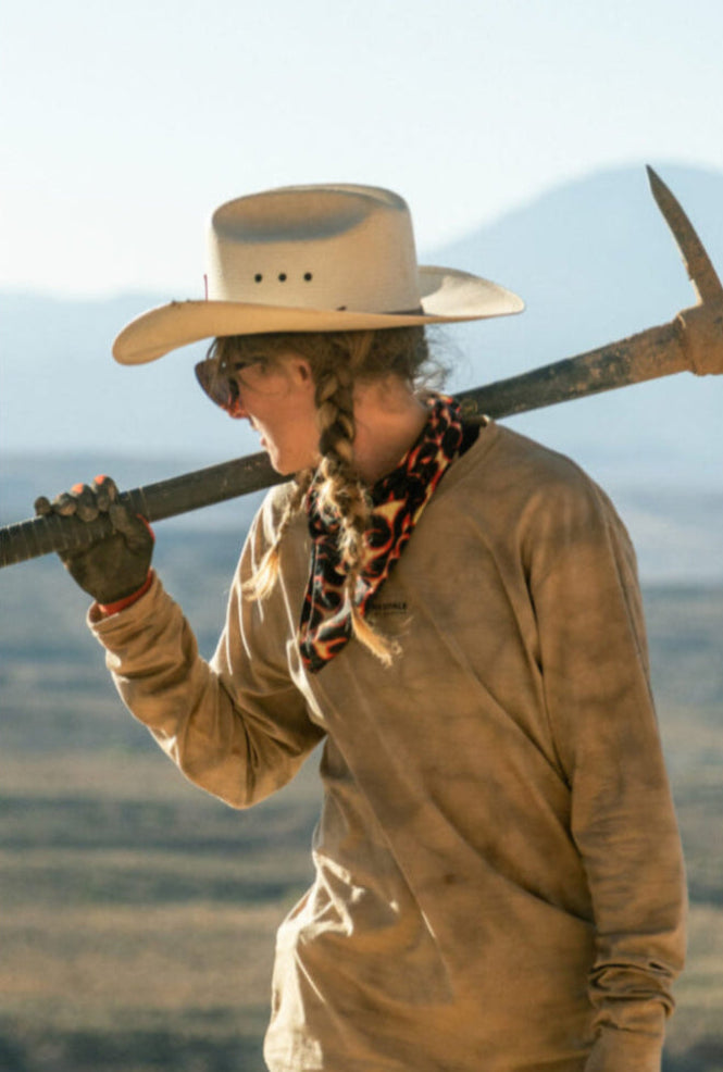 Casey Brown wearing a cowboy hat and holding a pick axe in the desert.