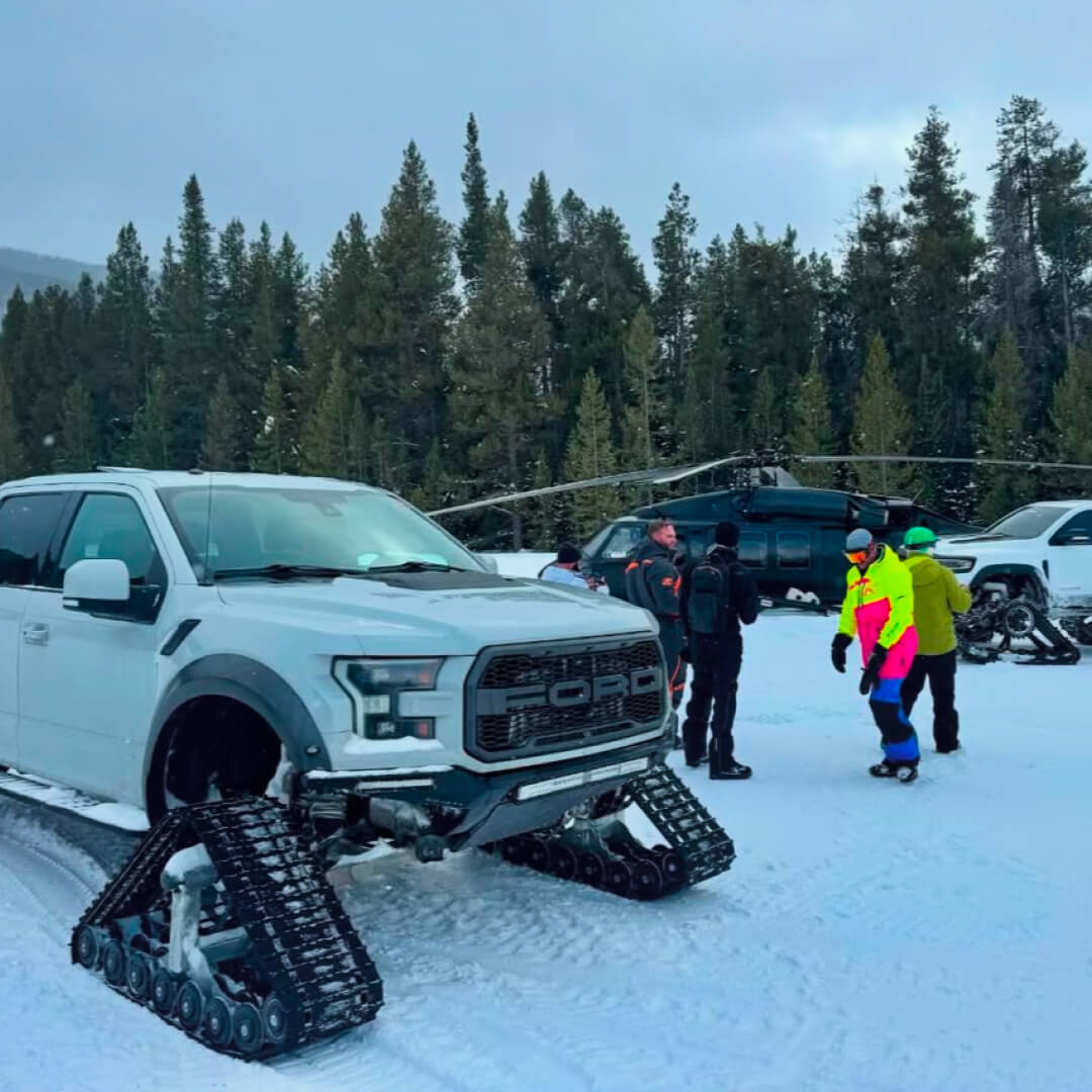 Chris' instagram photo of a Ford truck with snow tracks attached, in the background is a helicopter and a group of people standing in the snow.