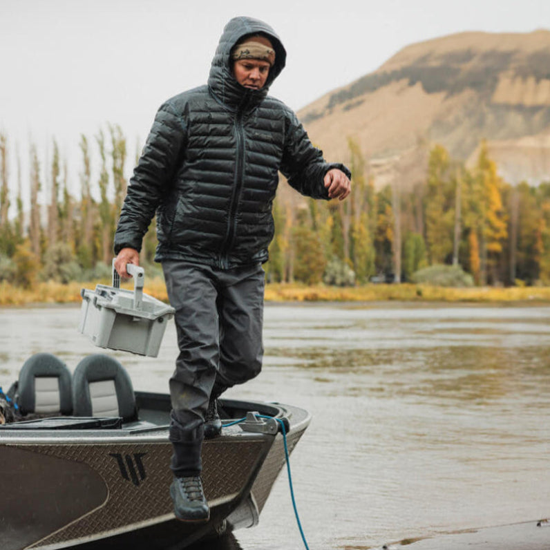 Curtis in outdoor gear stepping off a boat on a lake with mountains in the background