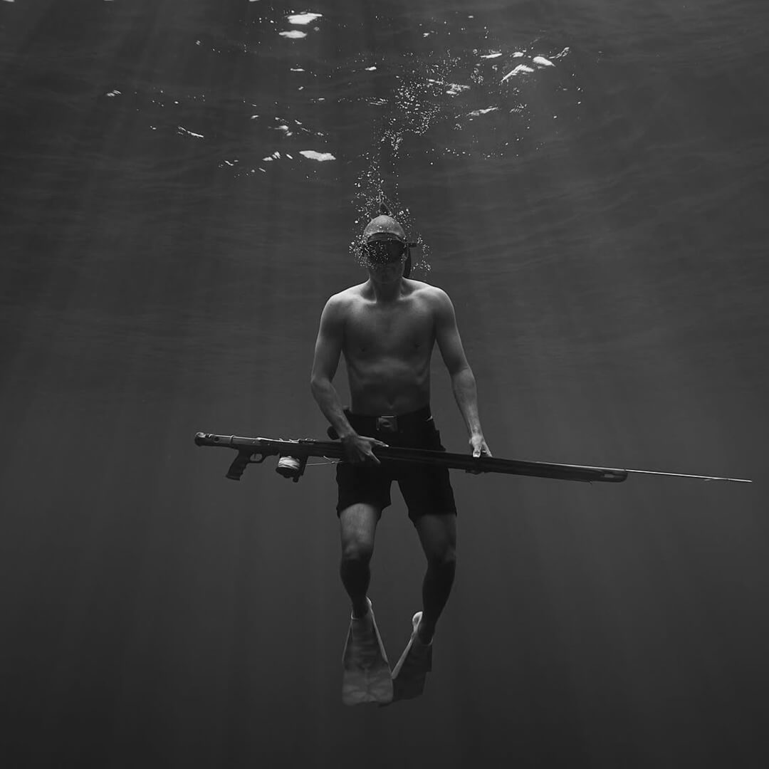 Danny Bolton and his speargun in black and white, floating just below the ocean's surface.