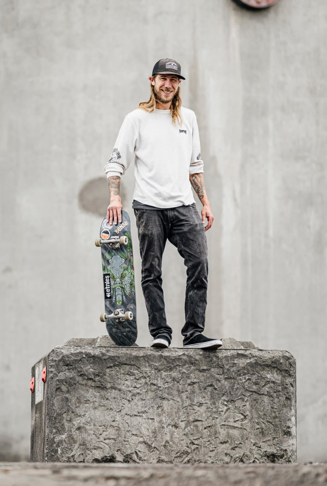 David Gravette holding onto his skateboard on a cement skate park feature.