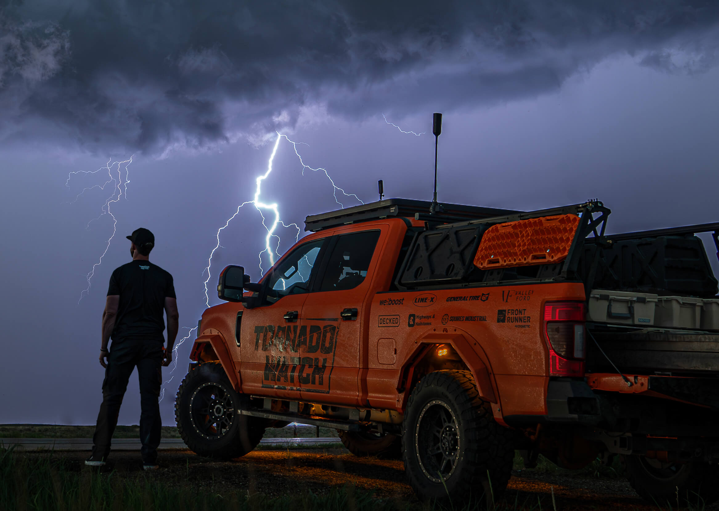 Ricky Forbes standing next to his storm chasing rig as lightning cracks on the skyline.