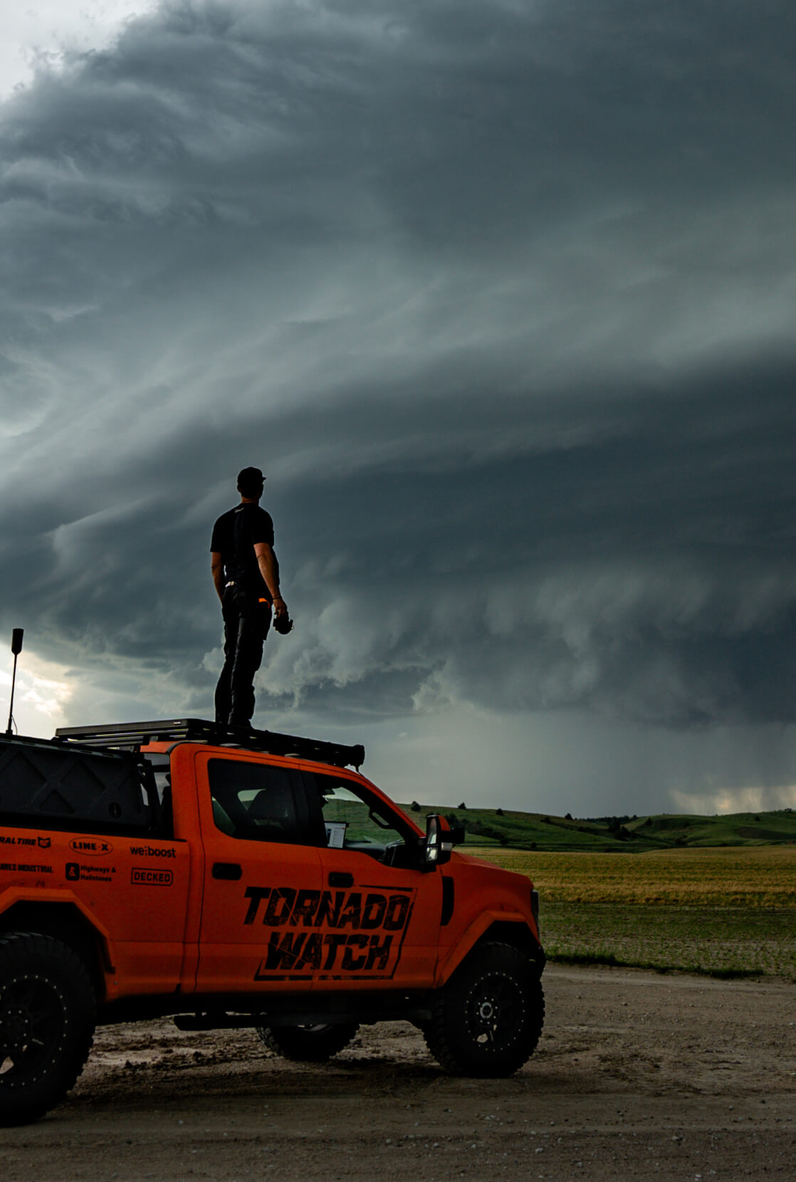 Ricky Forbes standing on top of his truck, looking across the plains at a budding tornado.