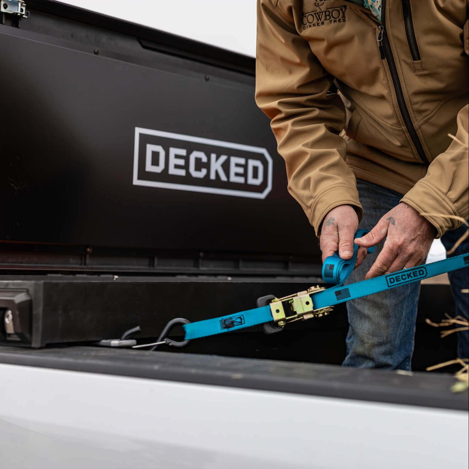 Person securing a DECKED blue Ratchet Strap to their DECKED Tool Box in order to lash down the cargo in their truck bed.
