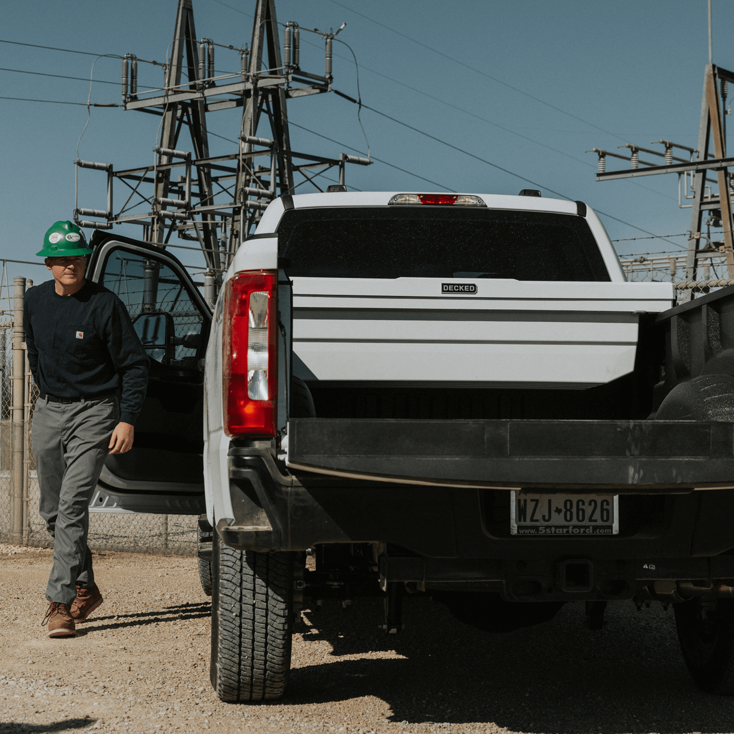Person standing next to a white truck with a white DECKED Tool Box with a clear sky background