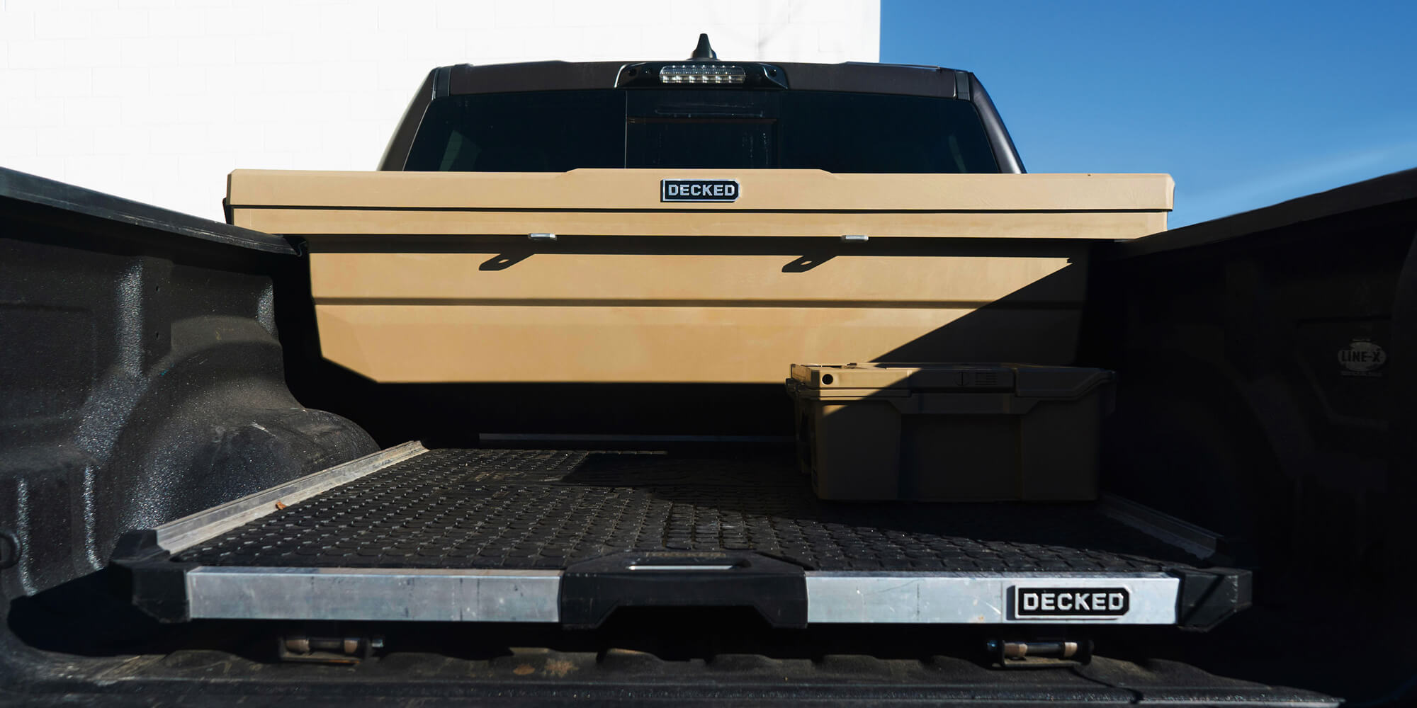 Truck bed with a DECKED Tool Box and CargoGlide storage system against a blue sky.