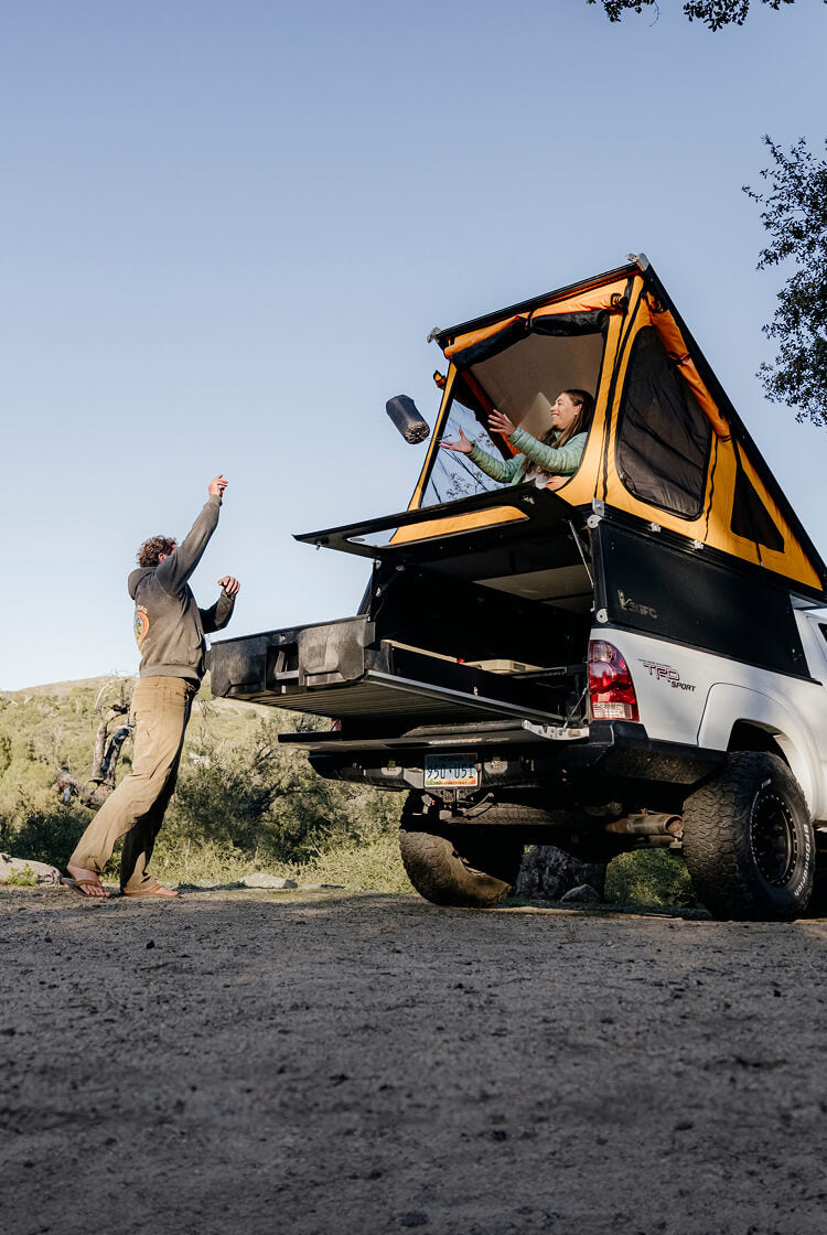 Two people tossing a sleeping pad from their Drawer System to their rooftop tent at their campsite.