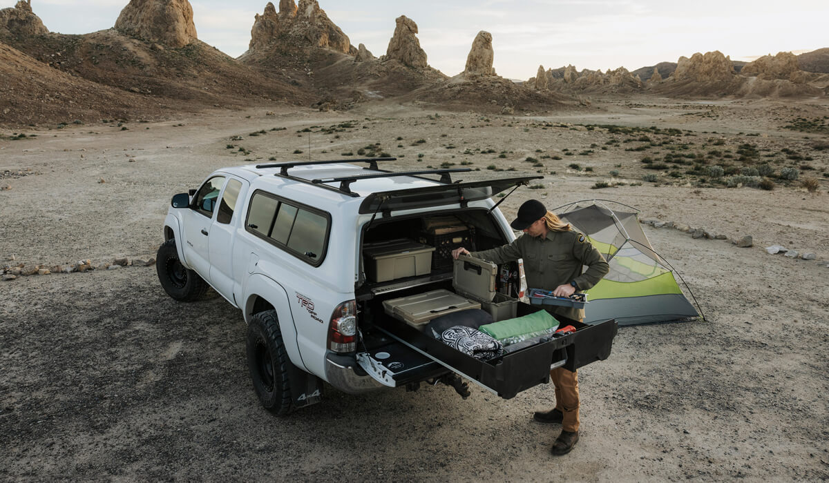 Person setting up a tent in the back of a white truck with a Drawer System in a desert landscape