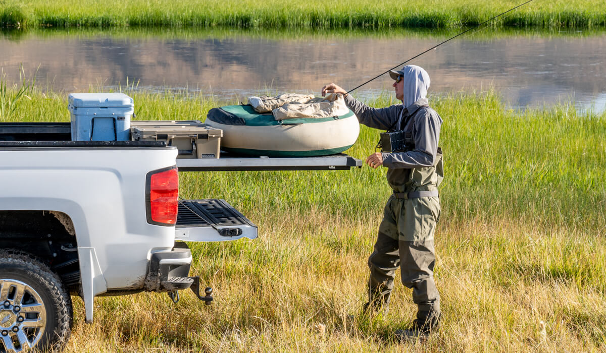 Man preparing to fish by a river with a truck with a CargoGlide sliding bed tray extended with a cooler and float on top.