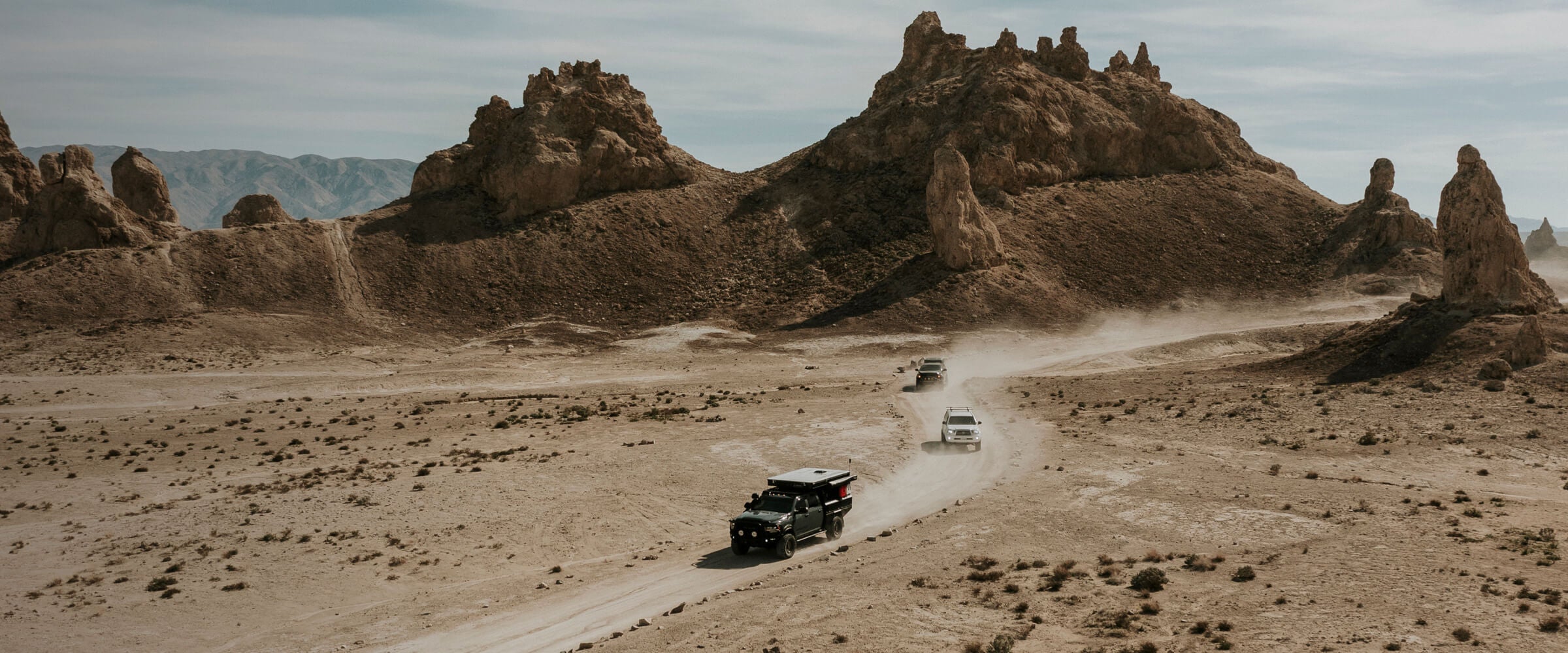 Desert landscape with rocky formations and vehicles on a dirt road.