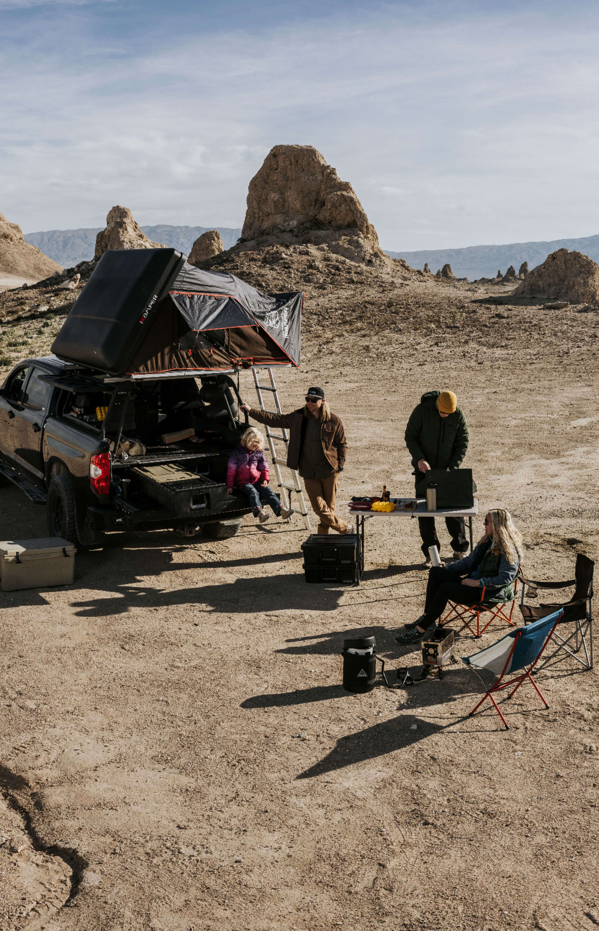 Group of people camping in a desert landscape with a truck outfitted with a Drawer System and outdoor furniture.