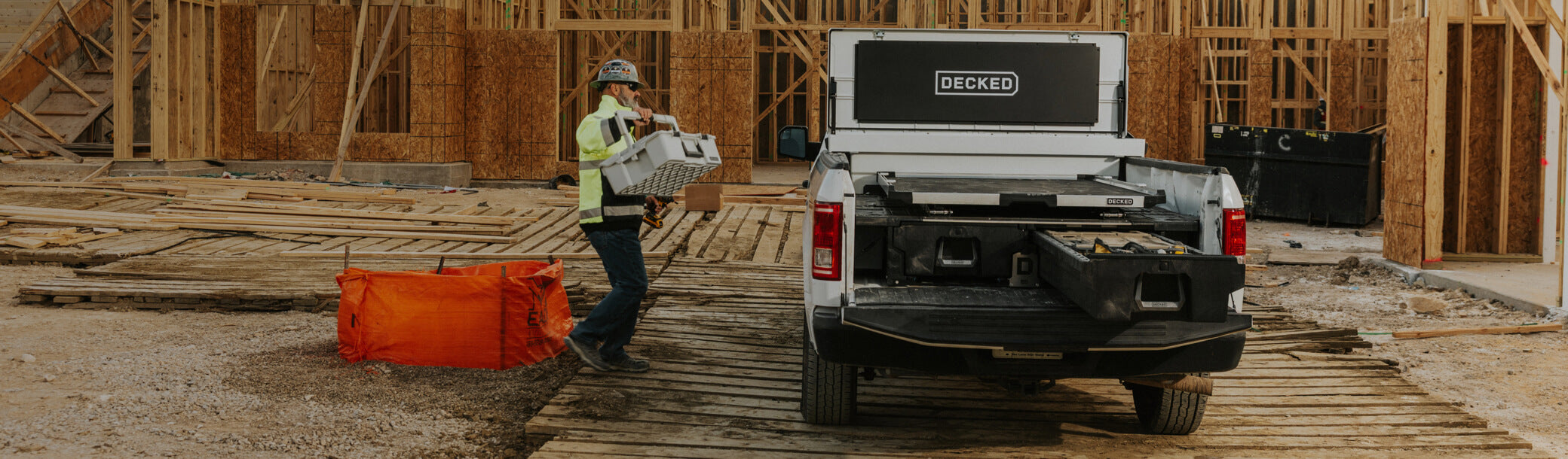 Construction worker loading a Halfrack into a truck bed equipped with 'DECKED' Drawer system, CargoGlide, and an open white Toolbox.