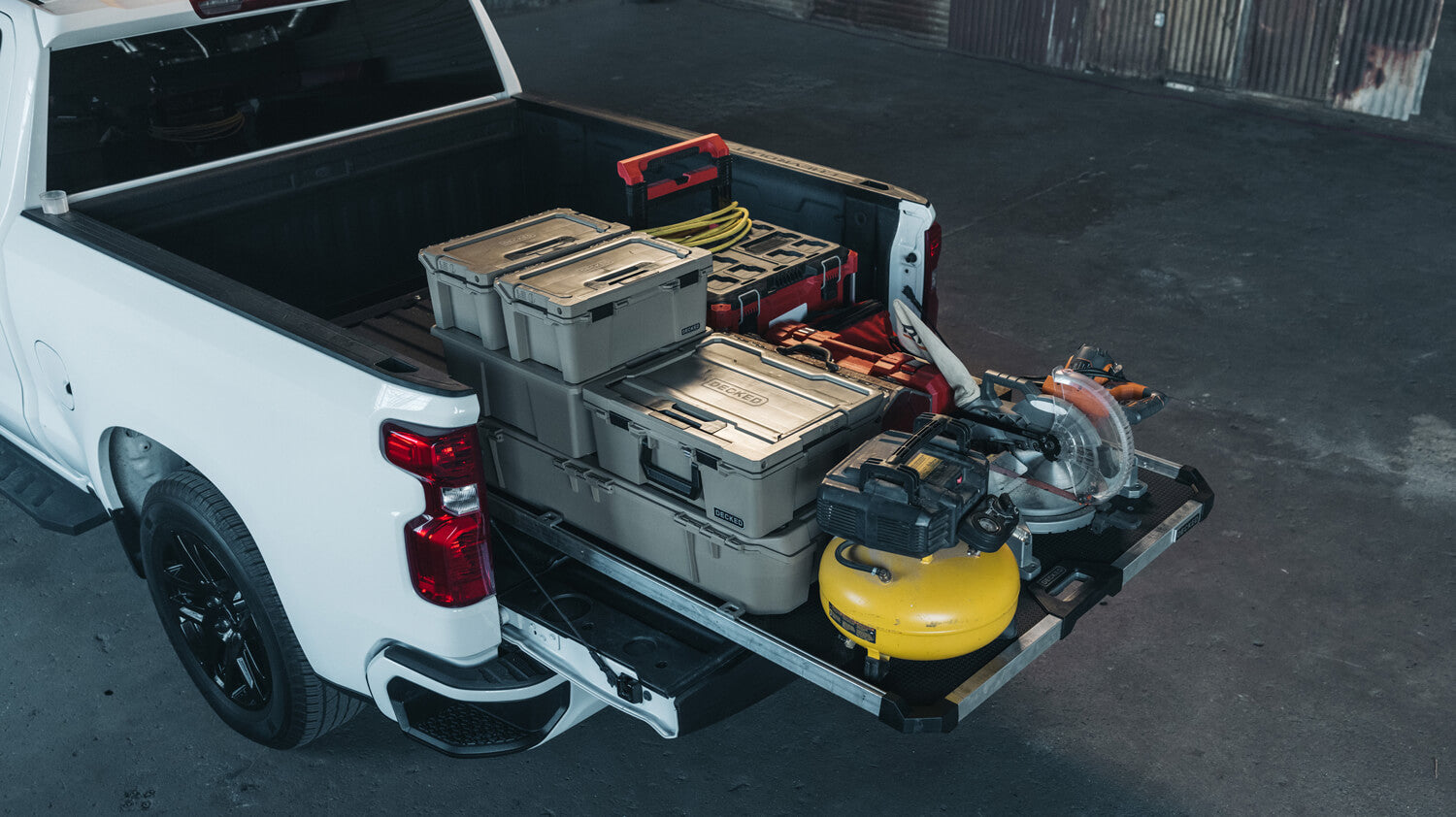A DECKED CargoGlide mounted with D-co cases and other tools n the bed of a white truck. 