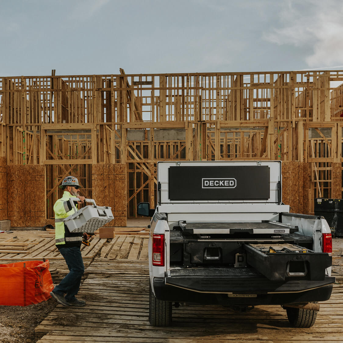Construction worker loading a DECKED Halfrack into a white DECKED Toolbox with a drawer system and CargoGlide mounted on top.